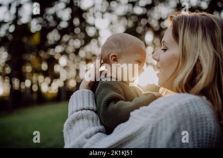 Mère tenant son petit fils portant un chandail tricoté pendant la marche dans la nature, regardant l'appareil photo. Banque D'Images