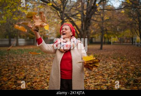 Bonne femme senior jetant des feuilles colorées dans les airs, profitant de l'heure d'automne. Banque D'Images