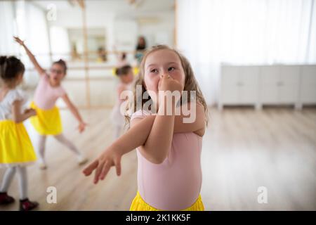 Petite fille avec le syndrome de Down imitant l'éléphant, s'amusant pendant le leson de ballet à l'école de danse. Banque D'Images