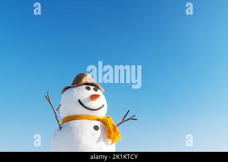 Bonhomme de neige drôle dans un élégant chapeau marron et jaune scalf sur un terrain enneigé. Ciel bleu sur fond Banque D'Images