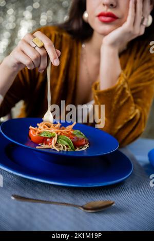 vue rognée de la femme floue tenant la fourchette près de l'assiette bleue avec spaghetti sur fond brillant, image de stock Banque D'Images