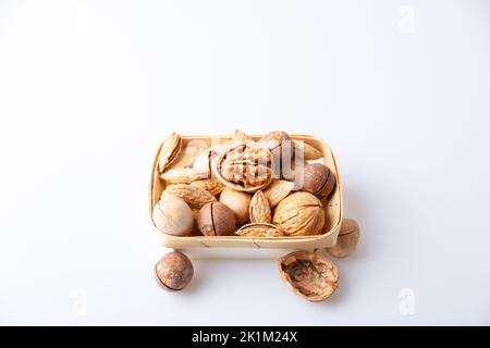 Noix assorties dans la coquille sur fond blanc : noix, pacanes, amandes, macadamia. Noix dans un panier. Mise au point sélective, gros plan. Placer pour le texte. Banque D'Images