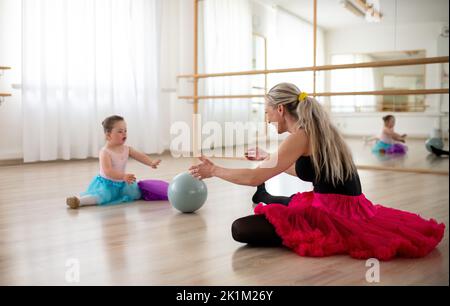 Petite fille avec le syndrome de Down jouant avec le ballon avec son lecteur de danse en studio de ballet. Banque D'Images