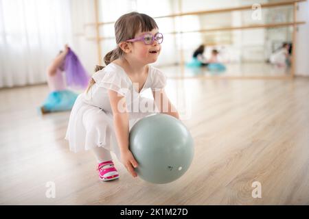 Petite fille avec le syndrome de Down jouant avec le ballon à la classe de ballet dans le studio de danse. Concept d'intégration et d'éducation des enfants handicapés. Banque D'Images