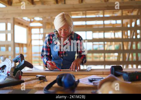 Femme senior manuel travaillant à l'intérieur de son écologique inachevé durable en bois éco-maison. Concept de femmes et de personnes âgées actives et indépendantes, éco Banque D'Images