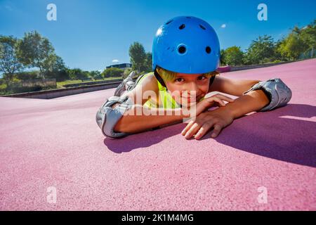 Un garçon en roller au skate Park se repose sur une surface colorée en souriant Banque D'Images