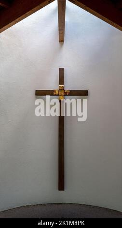 Croix de bois brun avec décoration d'or sur un mur blanc semi-circulaire avec incidence de lumière Banque D'Images