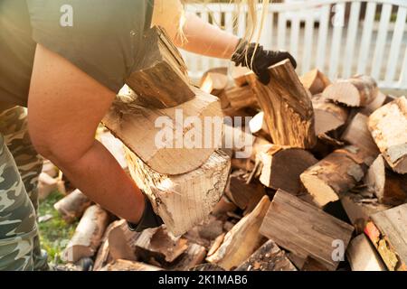 Une femme en vêtements décontractés recueille des billes de hêtre. Le bois de chauffage a été livré dans le jardin avant et est stocké sur une étagère pour l'hiver. Banque D'Images