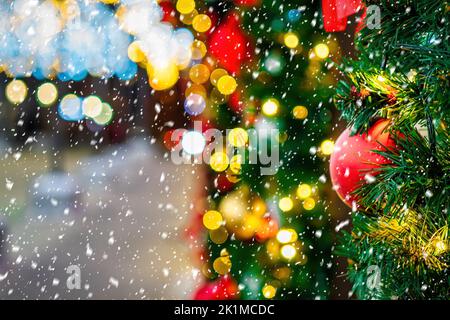 Boules de Noël, jouets et guirlandes brillantes sur une épinette artificielle avec de la neige qui tombe. Arrière-plan abstrait de Noël. Banque D'Images