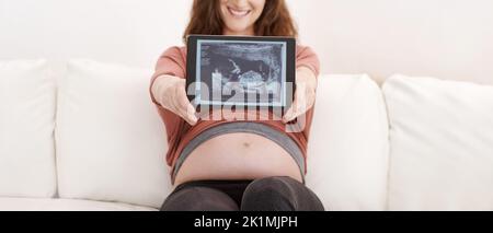 Bientôt disponible. Jeune femme enceinte luisant montrant son échographie sur une tablette numérique Banque D'Images