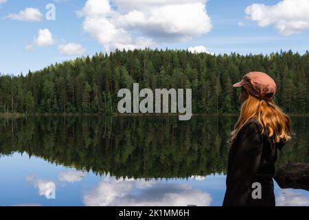 Femme aux cheveux rouges portant une casquette regardant le lac calme avec réflexion sur une belle journée d'été dans la nature Banque D'Images
