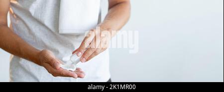 Hygiène masculine. Produit cosmétique. Traitement du visage. Mains d'homme méconnaissables verser le nettoyant à partir d'une petite bouteille transparente sur un tampon de coton isolé sur un em neutre Banque D'Images