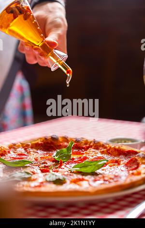 Huile d'olive déversant d'une bouteille sur une pizza Banque D'Images