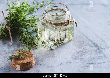 Huile de thym en bouteille, feuilles de thym vert sur fond gris Banque D'Images