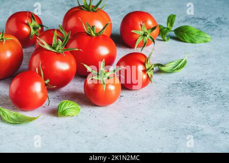 Tomates aux feuilles de basilic sucrées sur fond de béton gris, espace de copie Banque D'Images
