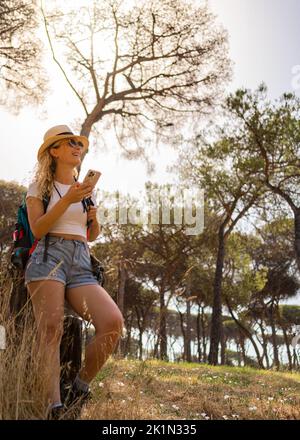 Femme entreprenante et heureuse explore dans la forêt avec son téléphone et son appareil photo, femme explorateur, plan vertical Banque D'Images