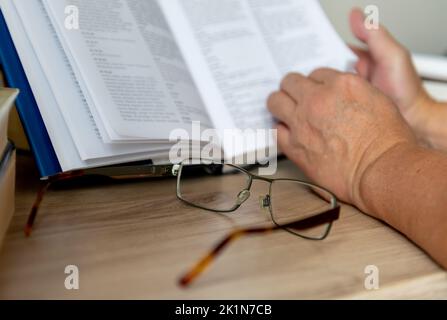 Une paire de lunettes sur un bureau avec une personne lisant un livre. Banque D'Images