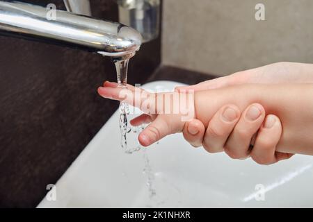 Femme mère lave les mains de bébé dans l'évier avec robinet. Maman aide avec l'hygiène enfant garçon. Enfant âgé d'un an et deux mois Banque D'Images