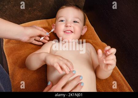 La mère nettoie l'oreille avec un coton-tige pour le bébé garçon heureux. Maman nettoie les oreilles d'un enfant souriant. Enfant d'un an Banque D'Images