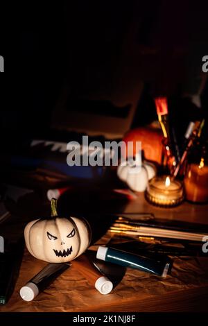 Halloween arts et artisanat. Peindre des citrouilles, des pinceaux et des peintures sur la table la nuit sombre. Gros plan de la citrouille peinte pour Halloween. Banque D'Images