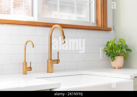 Un évier de cuisine avec un robinet en or, un évier à tablier, un fond de carreaux de métro et un meuble vert clair. Banque D'Images