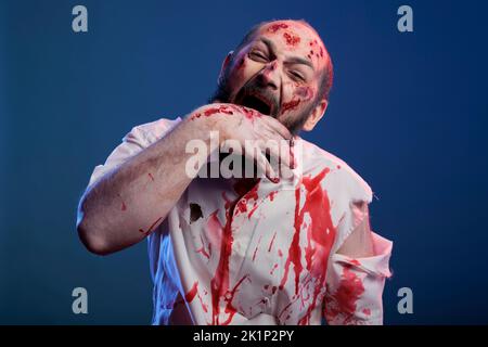 Halloween cruelle zombie piquant main avec des cicatrices et des blessures sanglantes, debout en studio. Un cadavre effrayant apocalyptique et un cerveau qui mangeait le méchant avec un visage d'horreur mortel et des yeux sinistres agressifs. Banque D'Images