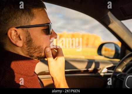 Un homme avec une barbe dans un chandail roule dans une voiture chère. Vue avant. Banque D'Images