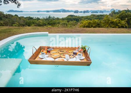 Plateau de petit-déjeuner flottant dans la piscine de l'hôtel de luxe ou de la villa tropicale, fruits, croissant, café et jus d'orange. Été exotique, détente Banque D'Images