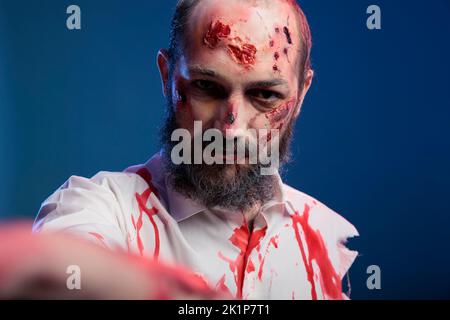 Zombie apocalyptique du diable avec des cicatrices sanglantes, mangeant le cerveau et regardant dangereux sur fond bleu. Monstre redoutable avec visage d'horreur et yeux de cadavre de mal créepy, méchant sinistre. Banque D'Images