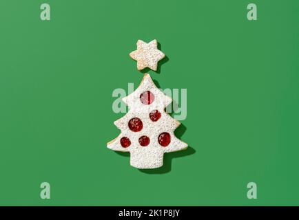 Vue ci-dessus avec un cookie en forme d'arbre de noël et une étoile. Délicieux biscuits linzer avec confiture de framboises, minimalistes sur une table verte. Banque D'Images