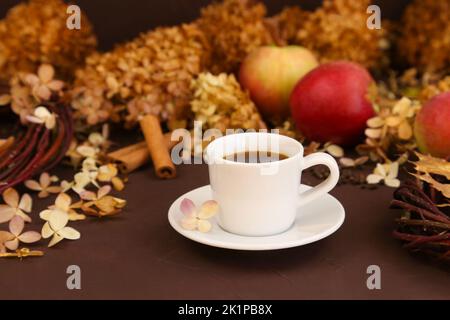 Tasse de café blanc, feuilles d'automne, cannelle, pommes et hortensia sec sur fond marron, vue de face. Mise au point sélective Banque D'Images