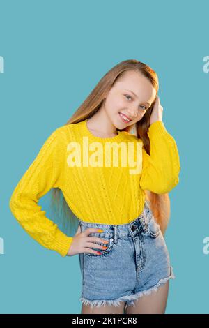 Portrait de bonne fille. Mode pour enfants. Look décontracté. Une enfance amusante. Jeune modèle gai en short de chandail jaune en denim posé isolé sur l'espace de copie bleu Banque D'Images