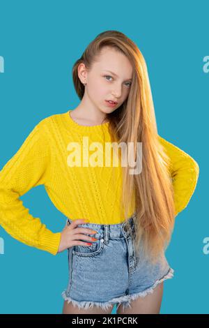 Mode pour enfants. Beauté décontractée. L'enfance moderne. Portrait de la jeune fille modèle confiante avec de longs cheveux justes dans jaune vif chandail Jean short standi Banque D'Images