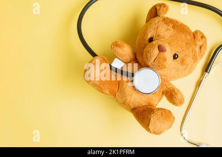 Stéthoscope avec poupée d'ours sur fond jaune pour soutenir la vie et la maladie des enfants. Septembre mois de sensibilisation au cancer chez l'enfant, soins de santé et vie Banque D'Images