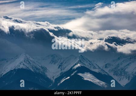 Une photo panoramique de hautes montagnes enneigées touchant des nuages épais à Fagaras, en Roumanie, pendant l'hiver Banque D'Images