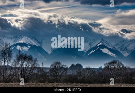 Une photo panoramique de hautes montagnes enneigées touchant des nuages épais à Fagaras, en Roumanie, pendant l'hiver Banque D'Images