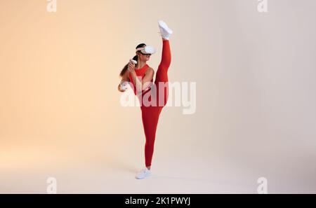 Une jeune femme sportive qui travaille dans la réalité virtuelle. Jeune femme sportive qui s'étire la jambe tout en s'engageant dans un jeu de remise en forme. Jeune femme active qui s'est lasse Banque D'Images