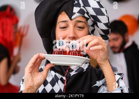 Femme habillée comme un arlequin mettant des boules de yeux sur la gelée rouge lors d'une fête d'Halloween. Banque D'Images