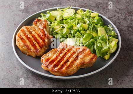 Viande épicée de porc grillé et salade verte avec choux de bruxelles, avocat et herbes dans l'assiette sur la table. Horizontale Banque D'Images