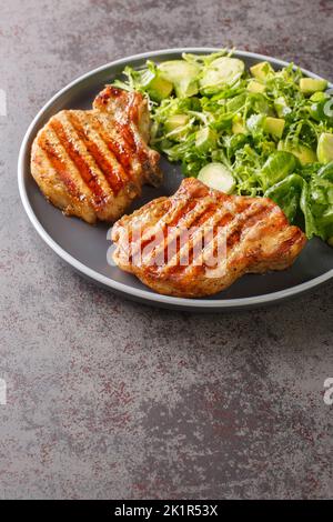 Côtelettes de porc grillées et salade de légumes verts avec choux de bruxelles, avocat et herbes dans l'assiette sur la table. Verticale Banque D'Images