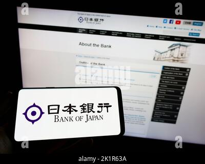 Personne détenant un smartphone avec le logo de l'institution financière Bank of Japan (BOJ) à l'écran devant le site Web. Mise au point sur l'affichage du téléphone. Banque D'Images