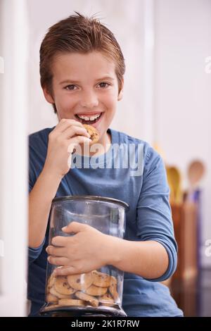 Tout pour moi. Un jeune garçon mangeant un cookie tout en tenant un pot à biscuits Banque D'Images