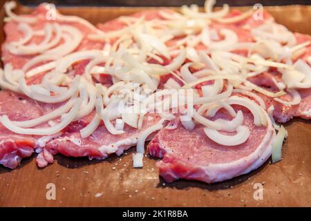 Côtelette de porc, filet de porc cru, tranché, arrosé d'oignons et placé sur une plaque de cuisson pour cuire au four. Banque D'Images
