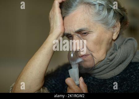 Femme âgée utilisant un nébuliseur fait l'inhalation à la maison. Banque D'Images