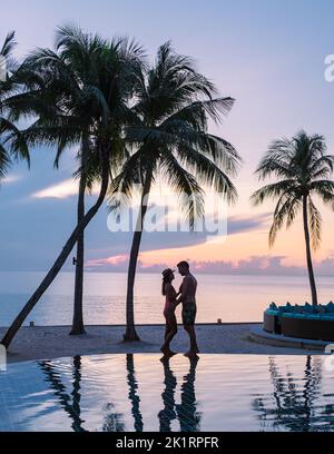 Deux hommes et femmes se détendent au bord de la piscine dans des chaises de plage, une piscine tropicale et une piscine avec des palmiers à la plage donnant sur l'océan Banque D'Images