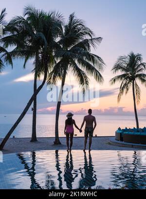 Deux hommes et femmes se détendent au bord de la piscine dans des chaises de plage, une piscine tropicale et une piscine avec des palmiers à la plage donnant sur l'océan Banque D'Images