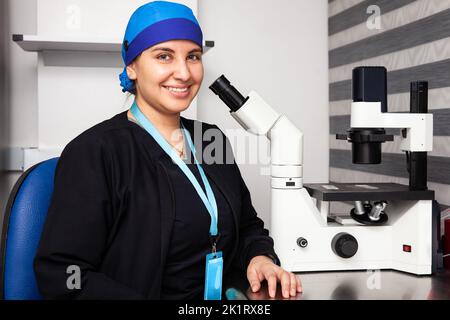 Belle jeune scientifique féminine dans le laboratoire à côté d'un microscope inversé Banque D'Images