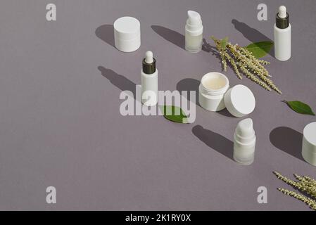 Maquettes blanches d'emballages cosmétiques et de plantes sur fond pastel avec espace de copie. Sérum, crème, lotion. Produit naturel de beauté et de soins de la peau confluent Banque D'Images