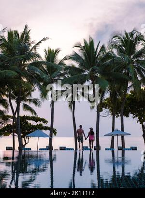 Deux hommes et femmes se détendent au bord de la piscine dans des chaises de plage, une piscine tropicale et une piscine avec des palmiers à la plage donnant sur l'océan Banque D'Images