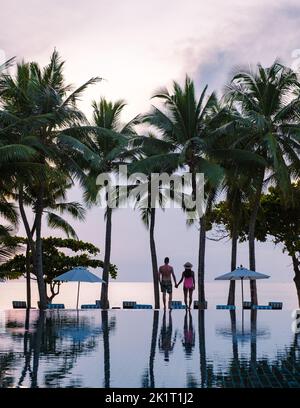 Deux hommes et femmes se détendent au bord de la piscine dans des chaises de plage, une piscine tropicale et une piscine avec des palmiers à la plage donnant sur l'océan Banque D'Images